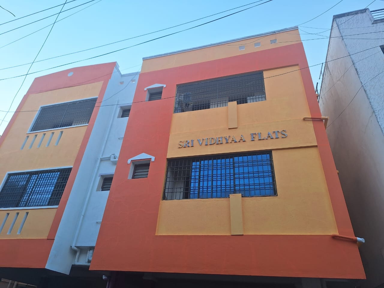 Photograph of Sri Vidhyaa Flats with its name on an ochre facade, terracotta bands and wide grilled windows